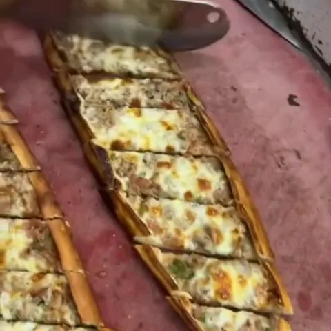 A cheese and minced-meat pide being sliced on the board