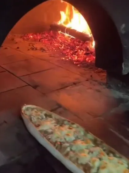 A minced-meat pide on the peel at the mouth of the wood oven